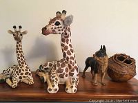 Four animal decor pieces arranged on a wooden surface against a plain wall: two giraffe sculptures, a bulldog figurine, and a wooden bowl with woven detail.