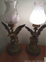 Pair of matching eagle table lamps with one lamp lit, showing frosted floral glass shades and detailed eagle bases.