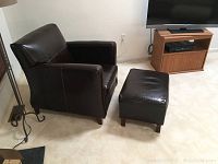 Side and angled views of dark brown leather Alexander Taylor chair with wooden legs and scratches/marks on surface.
