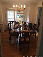 Six goldtone wood dining chairs arranged around table under overhead chandelier