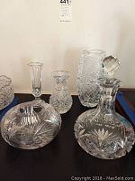 Photo of 4 cut glass vases and 1 cut glass decanter arranged on blue surface against white background.