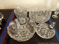 Four clear crystal servingware pieces arranged on a surface. Large, medium, and small serving bowls alongside a covered candy dish, all with detailed cut glass patterns.