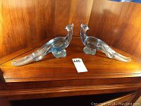 Pair of clear glass birds on wooden surface, front view