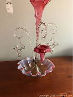Front view of the tall rose-colored glass decorative piece with three clear glass hanging elements on a ruffled pink and white base.
