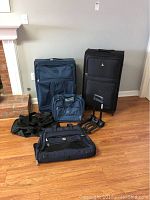 Image showing two large roller bags, duffel bag, clothes bag, roller briefcase, and dolly on wooden floor against gray wall.