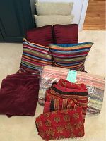 Eight assorted throw pillows arranged stacked with four folded blankets in front of them on carpeted floor.