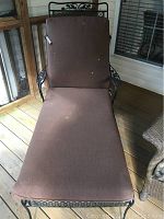 Front view of black wrought iron lounge chair with brown stained cushion on wooden deck