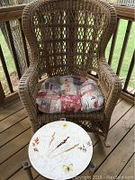 Wicker rocking chair with floral and Asian-themed cushioned seat and round side table with botanical leaf designs on top on wooden deck