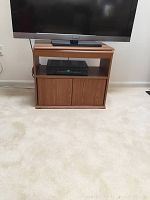 TV stand showing swivel top with flat screen TV placed on it and an electronic device on the open shelf below. Visible hole cut in the back for cords and cabinet doors below.