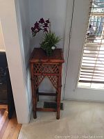 The bamboo corner table with faux flowering plant on top placed next to a door and wall corner.