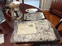 Photo showing 11-inch pewter decorative tray, silverplate pitcher, rectangular silverplate dish, and packaged Irish linen tablecloth on dark wood table.