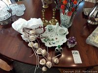 View of the Limoges dish with sugar and creamer cups, vintage white glass snuff bottle, brass candlesticks, glass vase with faux plants wrapped in white tissue paper, small purple flower figurine on wood table.