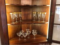 Shelf holding six clear glass water goblets with gold rims and seven clear crystal champagne glasses.