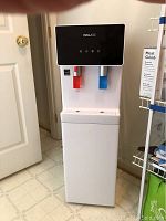 Full view of Newair white water cooler with bottom loading water bottle compartment, red hot water and blue cold water taps under black control panel.