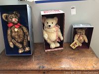 Photo showing three Steiff bears in original boxes against white background on a wooden surface.