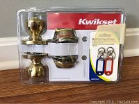 Kwikset branded door knob set model 79984 in original packaging, brass finish knobs and trim, includes 3 key tags in red, blue, and white with key rings.