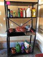 Photo showing a black metal shelving unit in a garage holding various gardening and pest control products including spray cans, spray bottles, extension cord, gloves, and bags of orchid bark and fertilizer.