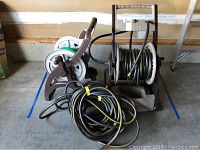 Two brown plastic garden hose caddies with winding handles; one caddy with black and yellow-striped hose wound on it, two separate black and yellow-striped garden hoses coiled on floor