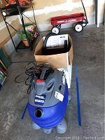 Shop-Vac Super Hawkeye shop vac showing overall unit in blue and gray plastic with power cord and hose attached, placed on blue tape lines on concrete floor.