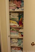 Full view of linen closet with multiple shelves filled with folded linens, towels, sheets and throws in different colors and patterns.