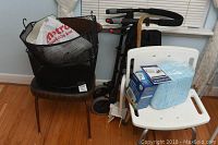 Photo showing the vintage wooden and metal chair with black vinyl upholstery, black metal mesh hanging basket on seat, and black walker behind.