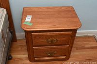 Front view of a Shermag oak nightstand showing two drawers with ornate metal pulls, natural wood grain visible.