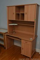 Full view of faux wood desk with upper hutch, desk lamp on top, and main desk surface showing its design and construction.