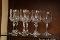 Front view showing five assorted lead crystal stemware glasses with cut designs on a glass shelf.
