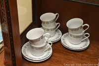 Four white porcelain teacups stacked with matching saucers showing a gold floral pattern around the rim.