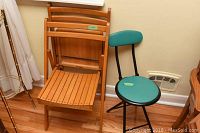 Two wooden folding chairs and one teal vinyl padded metal folding chair arranged against a wall on a hardwood floor.