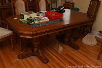 Full view of oak wood rectangular dining table showing the whole tabletop with various items on top and the pedestal legs beneath.