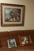 Peacock motif print in large gilt wood frame hanging above couch with two smaller framed prints placed on couch below