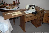 Singer sewing machine mounted in wooden cabinet with fold-out extension showing wooden grain and metal drawer pulls.