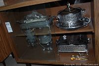 Photo showing glass cabinet with various silver plated trays, serving bowl, water jug and napkin ring holders arranged on shelves.