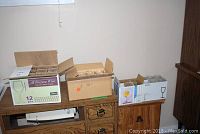 Four boxes filled with various glassware placed on wooden furniture against a white wall.