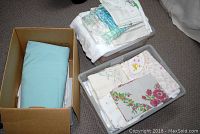 Photo of a cardboard box and two plastic bins filled with folded linens of various colors and patterns.