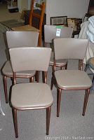 Four vintage chairs with light tan vinyl upholstery and copper-colored metal frames arranged together in a room.