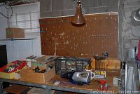Overview of workbench with wooden hardware cabinet, pegboard, tools on the surface, and hanging adjustable lamp
