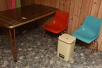 Full view of vintage kitchen table with melamine top and 2 plastic molded chairs in red and blue, plus metal pedal waste bin