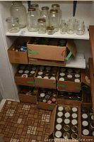 Shelf with assorted large and small glass preserving jars, some with metal lids, visible wear and use. Includes a glass jar with clamp lid.
