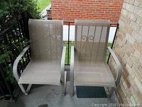 Photo showing front and side view of two metal frame garden chairs with mesh seating placed next to outdoor brick wall and railing.