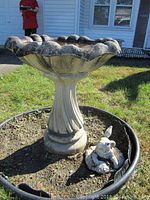 Concrete birdbath in outdoor garden setting, showing scalloped edge and column pedestal, weathered surface