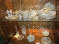 Shelf showing a variety of crystal items including swan figurines, napkin holder, small vases, handbells, and decorative dishes.