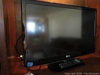 Front view of the LG 26-inch flat screen TV with remote on the stand, showing the screen and frame.