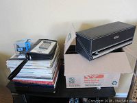 View of stacked LP albums with CD cases and Bluetooth speaker on top, displayed next to a cardboard box.