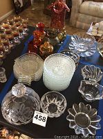 Full view of collection on table with variety of clear crystal glass items, colored glass vases and pitchers in amber and red-orange tones, stacked plates and bowls