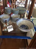 Full view of the lot in a glass display cabinet including the large bowl, smaller bowls stacked, and the figurine.
