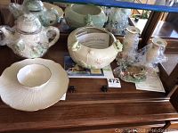 Photo of white porcelain serving dish with raised leaf pattern and 24 karat gold rim, surrounded by frog-themed figurines including a teapot, candlesticks, and bowl, some wrapped in plastic with paperwork visible.