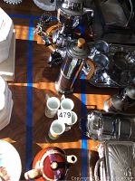 Overview of lot showing coffee maker, chrome thermos, three floral demi cups, brown ceramic teapot and assorted metal serving pieces.