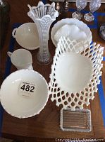 Overview of various milk glass items including pitcher, bowls, and centerpiece bowl with lattice edge on a wooden table.